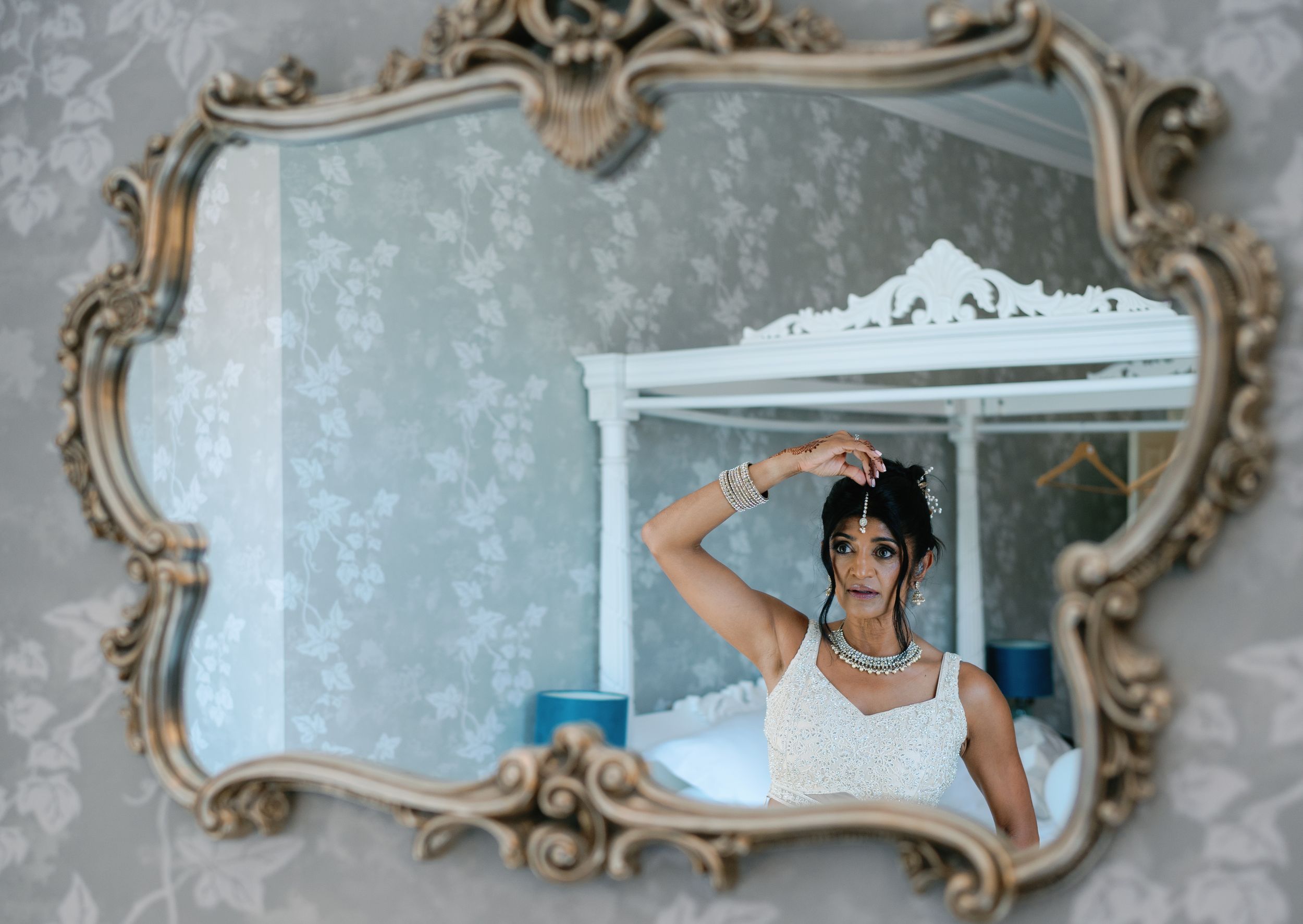 A reflection in an ornate mirror shows someone adjusting their wedding attire.