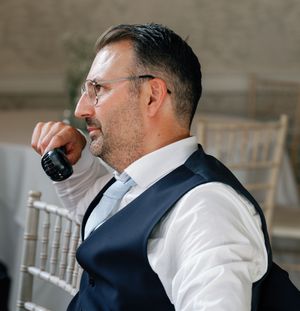 Side profile of a person in a white dress shirt and vest speaking into a microphone.