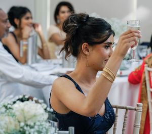 Guest in navy dress raising a champagne glass during wedding reception toasts.