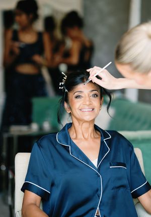 A person in a navy blue pajama-style top smiles while getting their hair styled during wedding preparations.