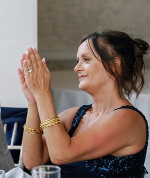 Guest in a navy dress with gold bracelets clapping at a celebration.