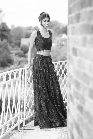 Black and white portrait of someone in an elegant two-piece evening gown on a balcony.