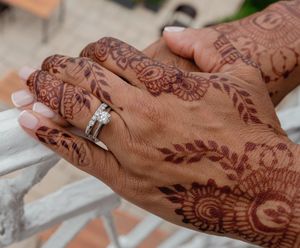 Close-up view of intricate henna designs on hands with a diamond engagement ring.
