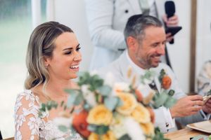 Wedding reception guests enjoy an outdoor dinner celebration with fresh flowers and yellow decor at sunset.