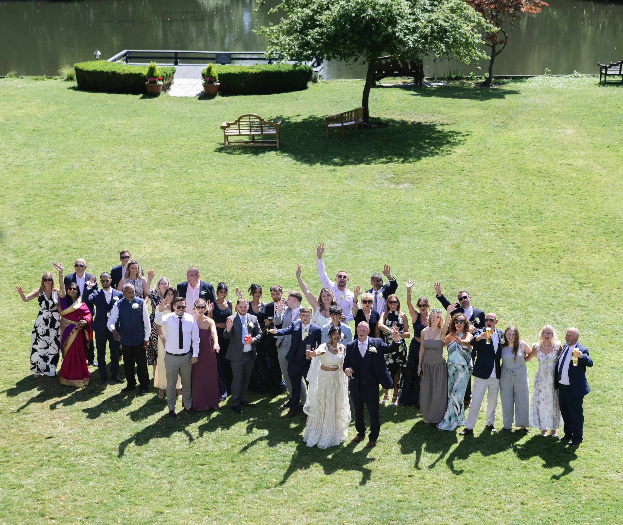 Wedding party gathered on a green lawn forming a group cheering pose with raised arms.