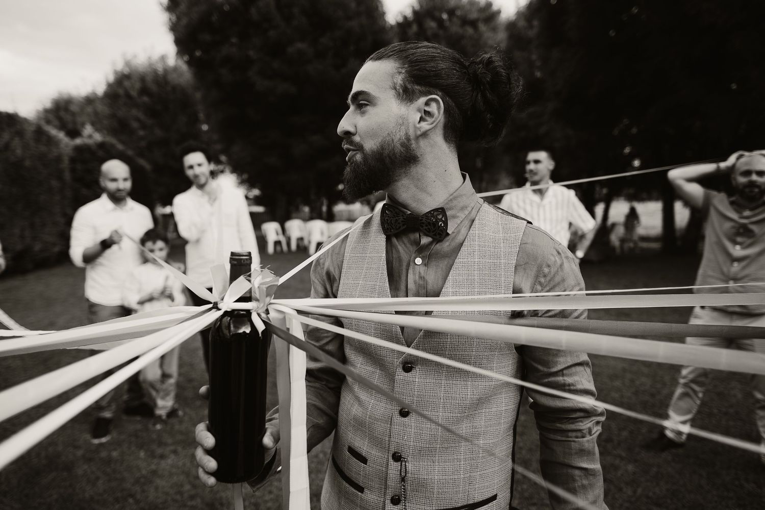 A black and white photo of guests at a wedding celebration with decorative streamers being held outdoors.