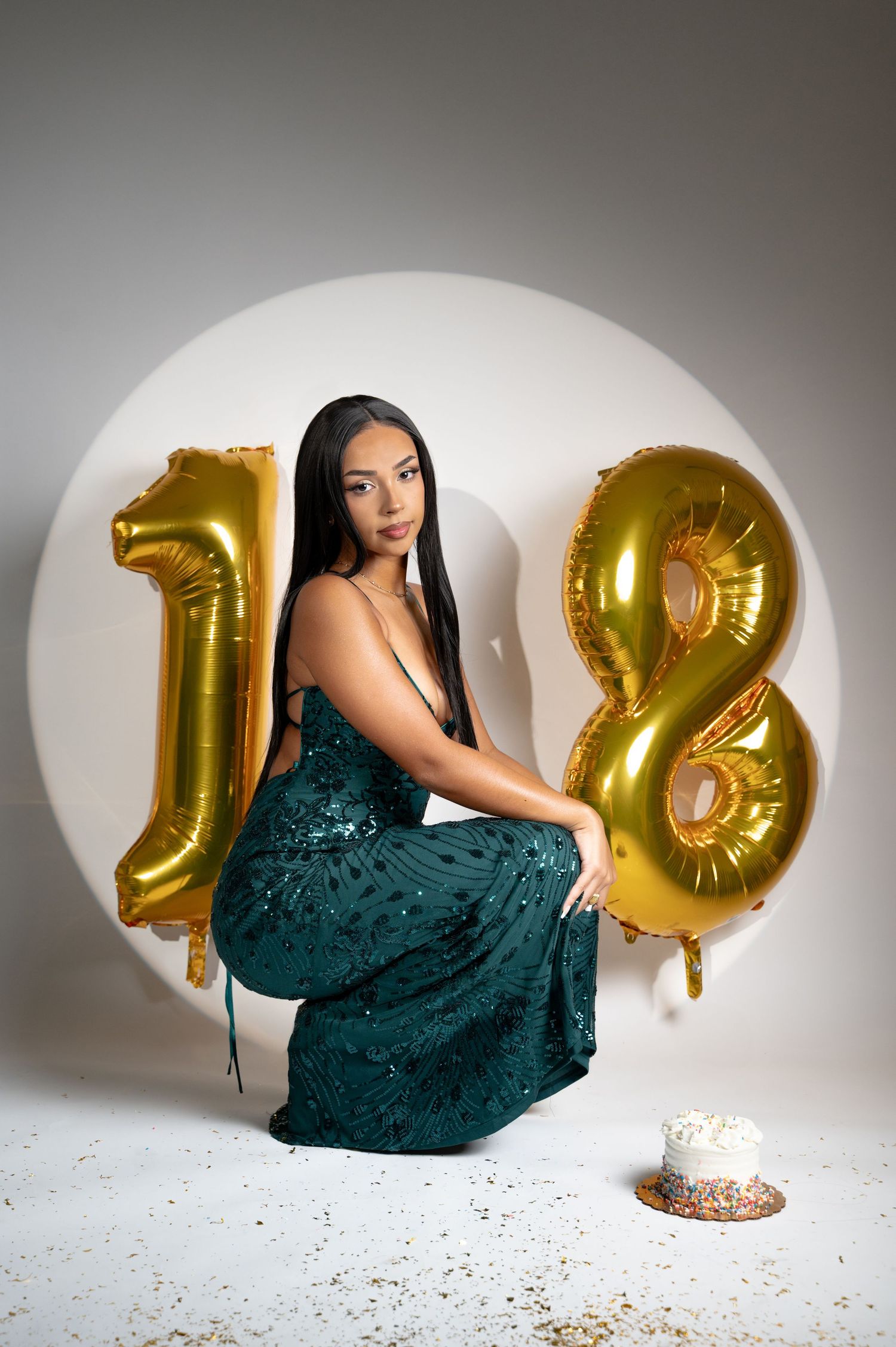 A teal sequined dress is photographed against a white backdrop with gold number balloons showing 18.