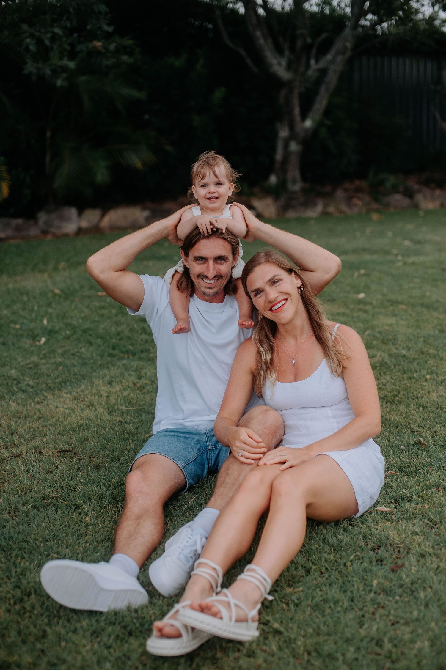 A playful couple sits together on grass while making funny faces and taking casual outdoor photos in summer.