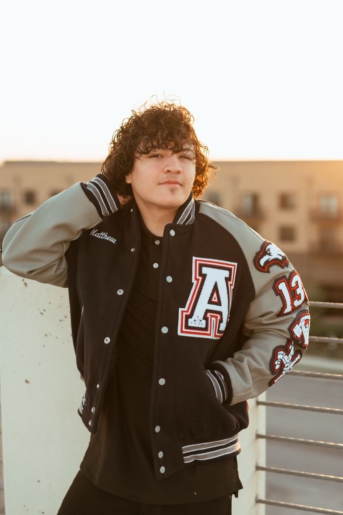 A sporty varsity letterman jacket with A patch shown at sunset against urban building backdrop.