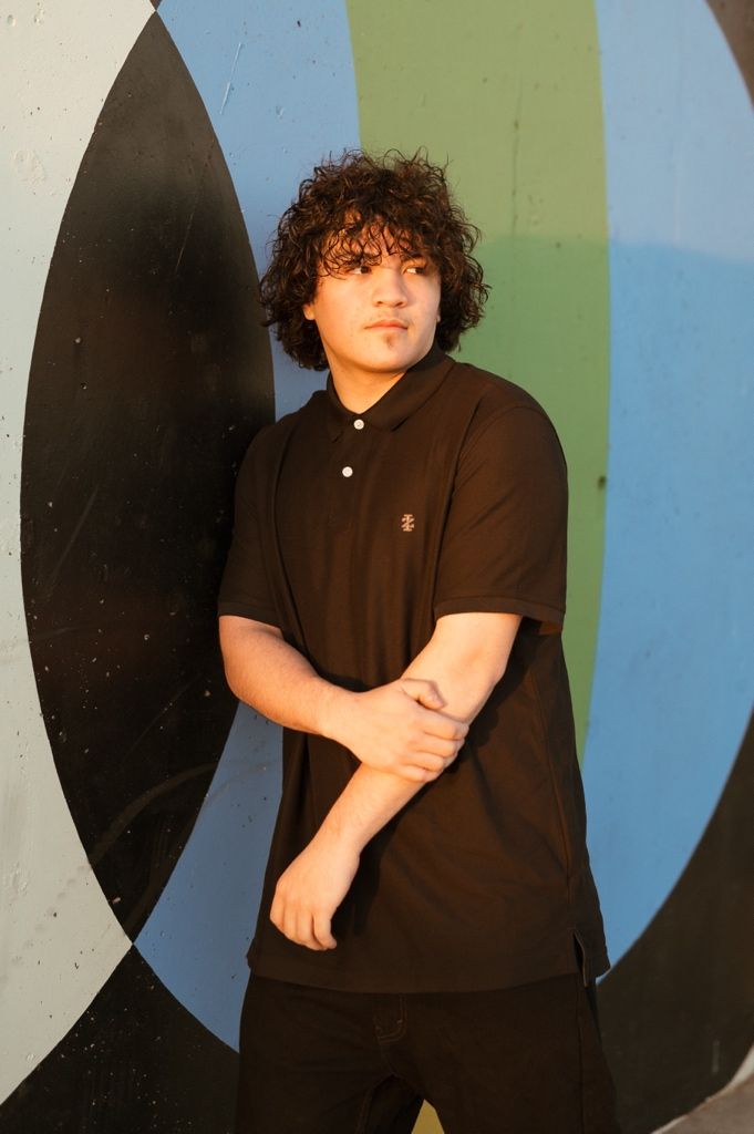 A figure in a black outfit stands against a wall with geometric shapes painted in blue and green tones.