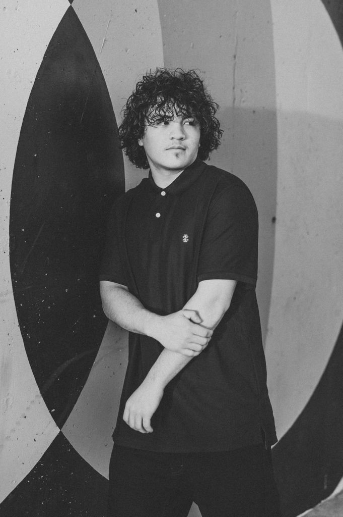 A black and white photo of someone in a dark outfit posing against a geometric patterned background.