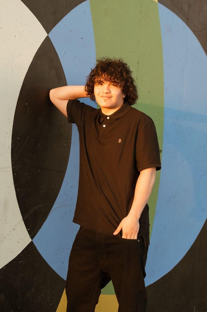 Figure in a dark shirt poses against a geometric wall mural featuring curved blue and green shapes.