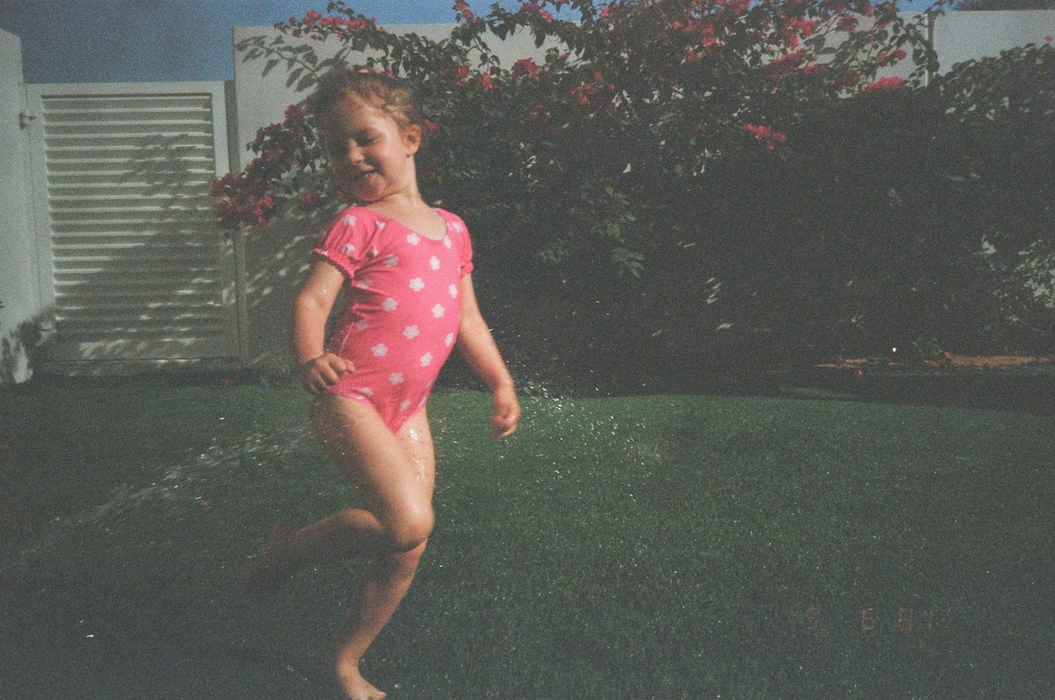 A child in a pink swimsuit runs and plays on green grass during a summer day.