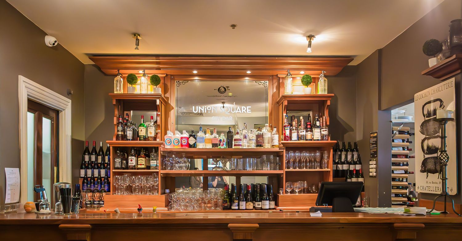 Wooden bar counter with illuminated shelves displaying liquor bottles and wine in a warm-lit restaurant interior.