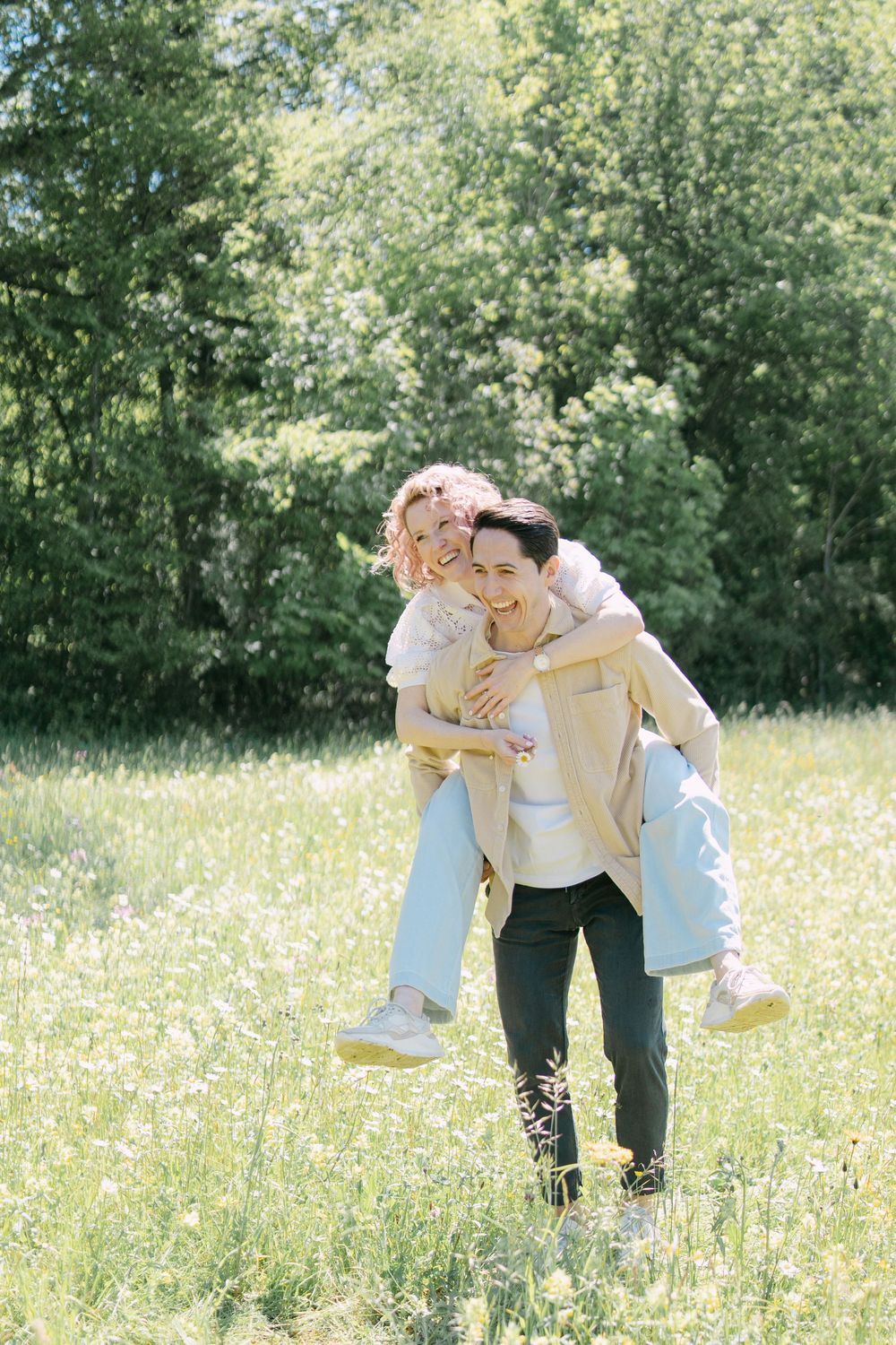 A playful piggyback ride in a sunny wildflower meadow surrounded by green trees on a bright summer day.