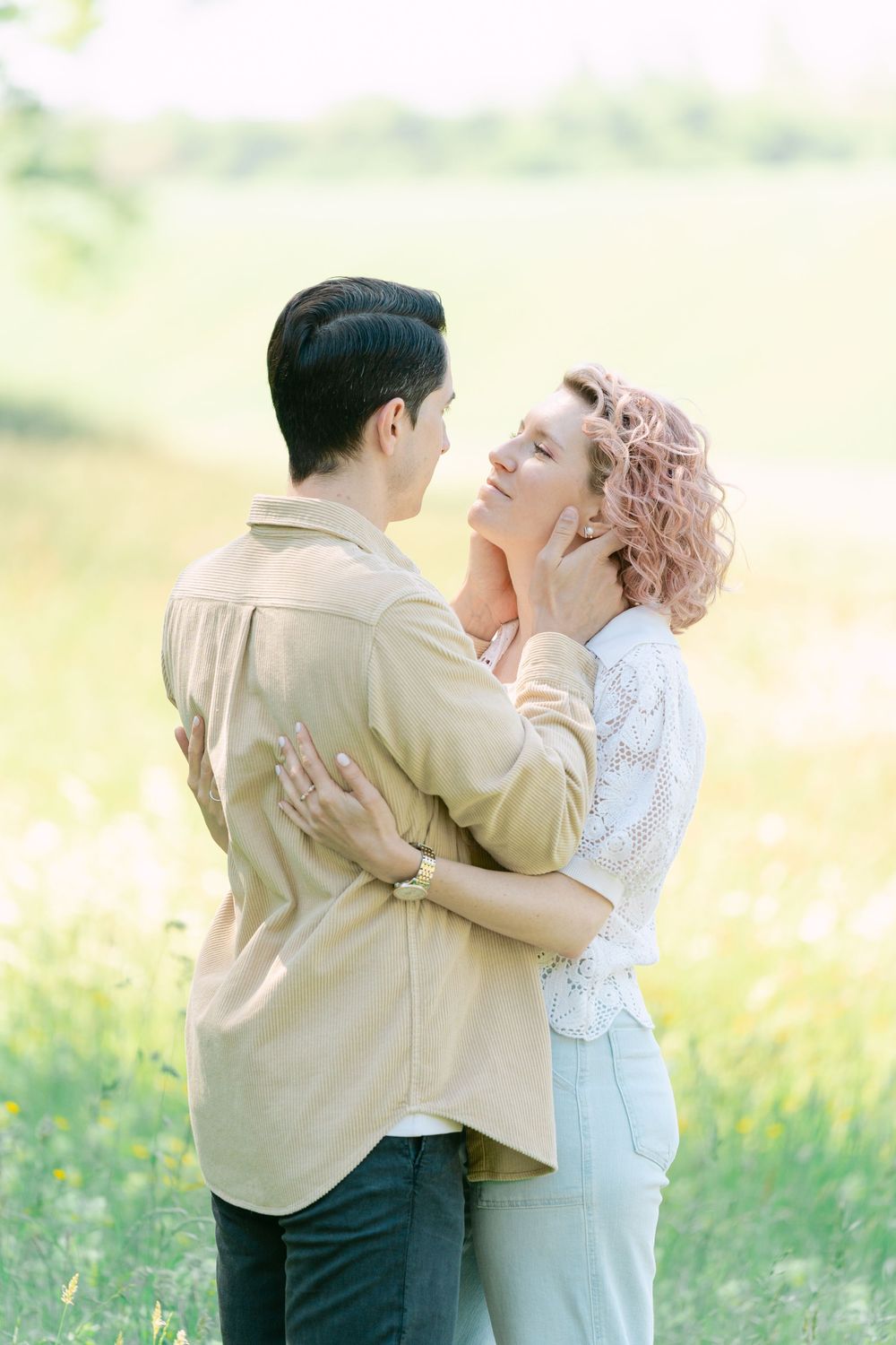 Romantic couple embrace in sun-drenched meadow wearing vintage-inspired attire.