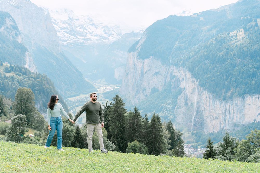 People holding hands on a green hillside overlooking dramatic mountain cliffs in the Swiss Alps on a sunny day.