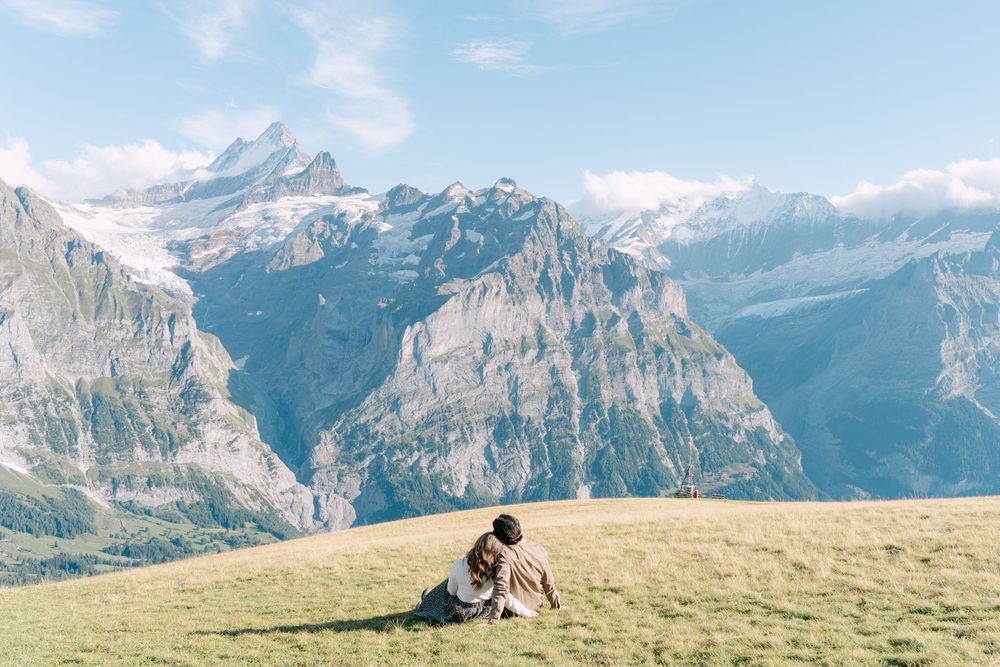 People sit on a grassy meadow overlooking stunning snow-capped mountains in the Swiss Alps.