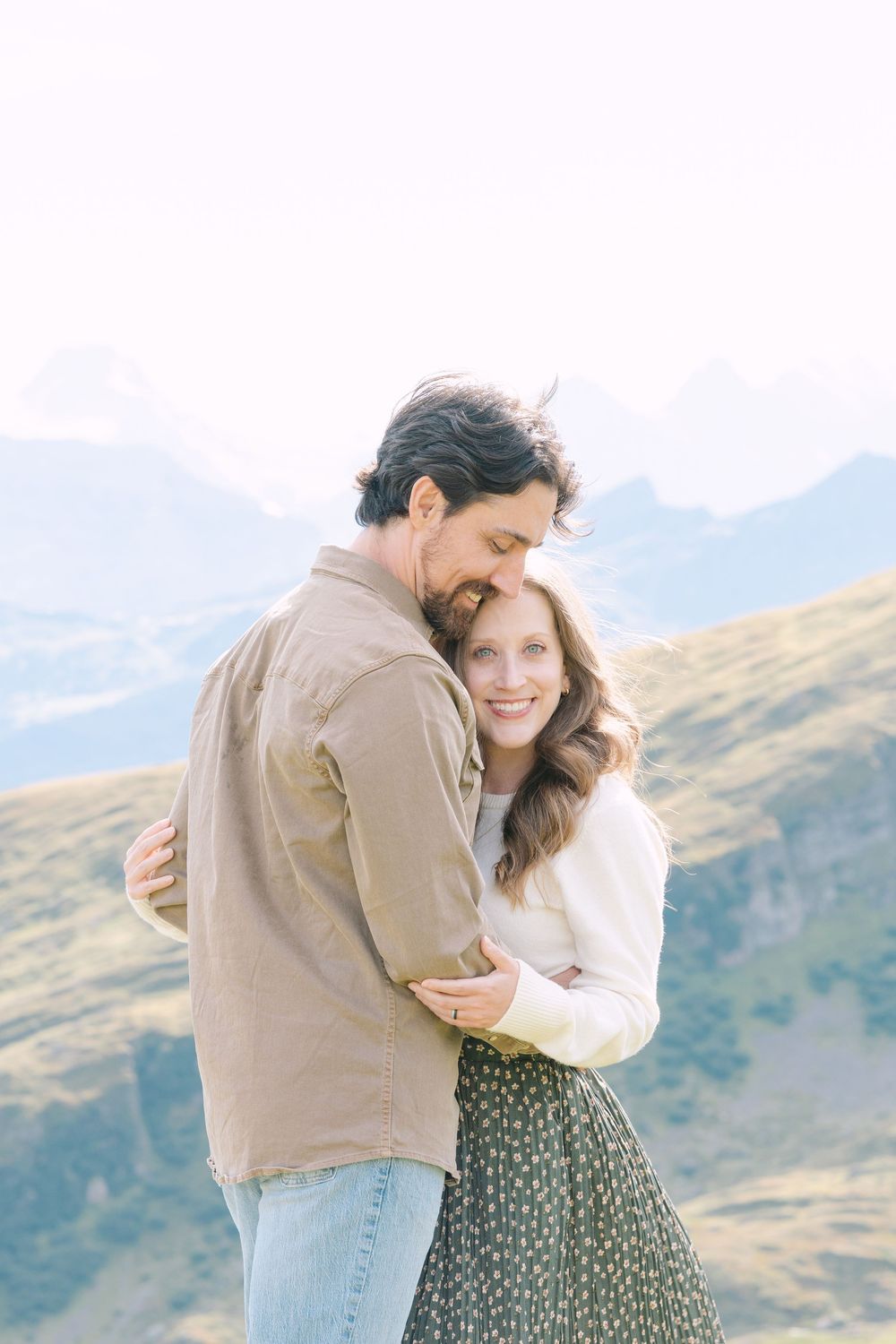 A couple embraces while standing in front of scenic mountain views on a sunny day.