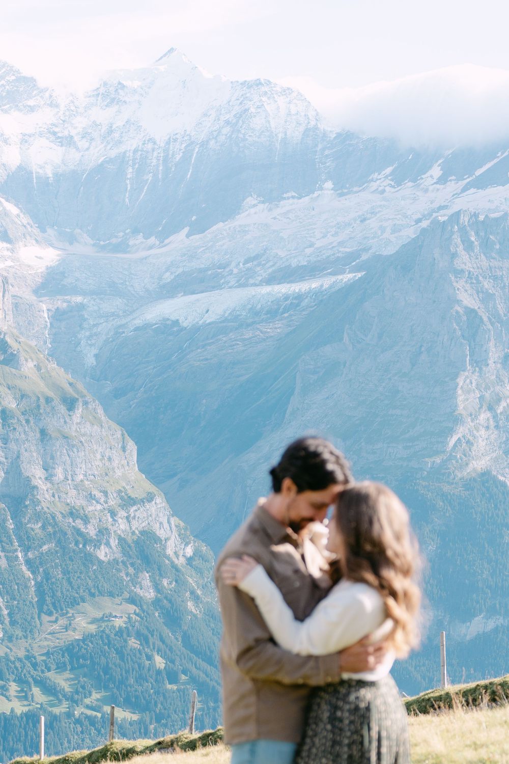 A couple embracing on a mountain meadow with majestic snow-covered Alpine peaks in the background.