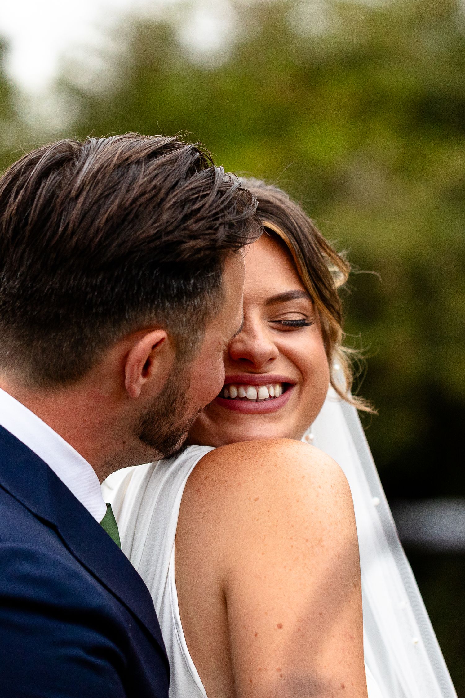 Two newlyweds share an intimate moment outdoors as they smile and embrace on their wedding day.
