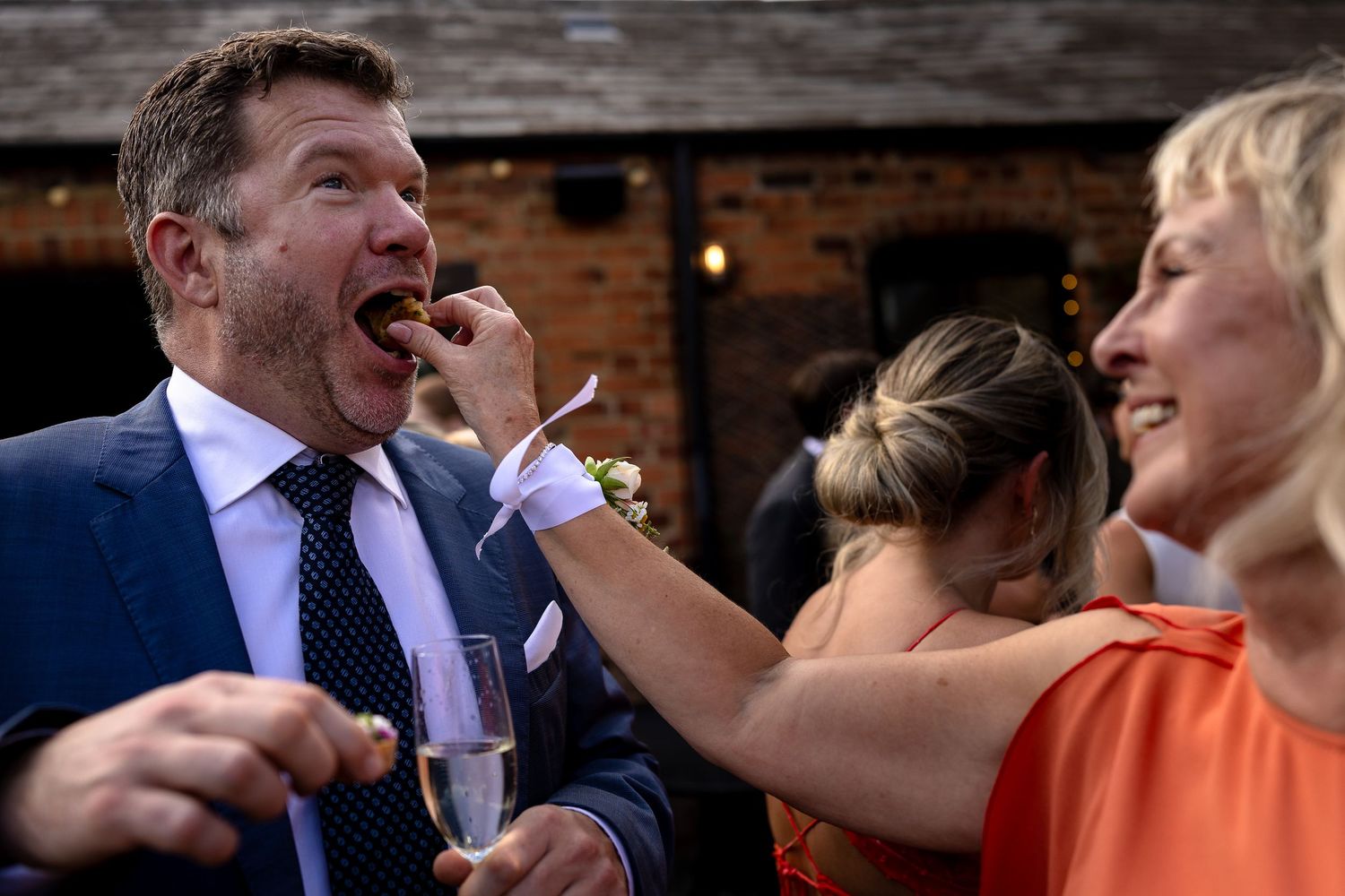 People celebrate at a party with one being fed a bite of food while laughing at an indoor venue.