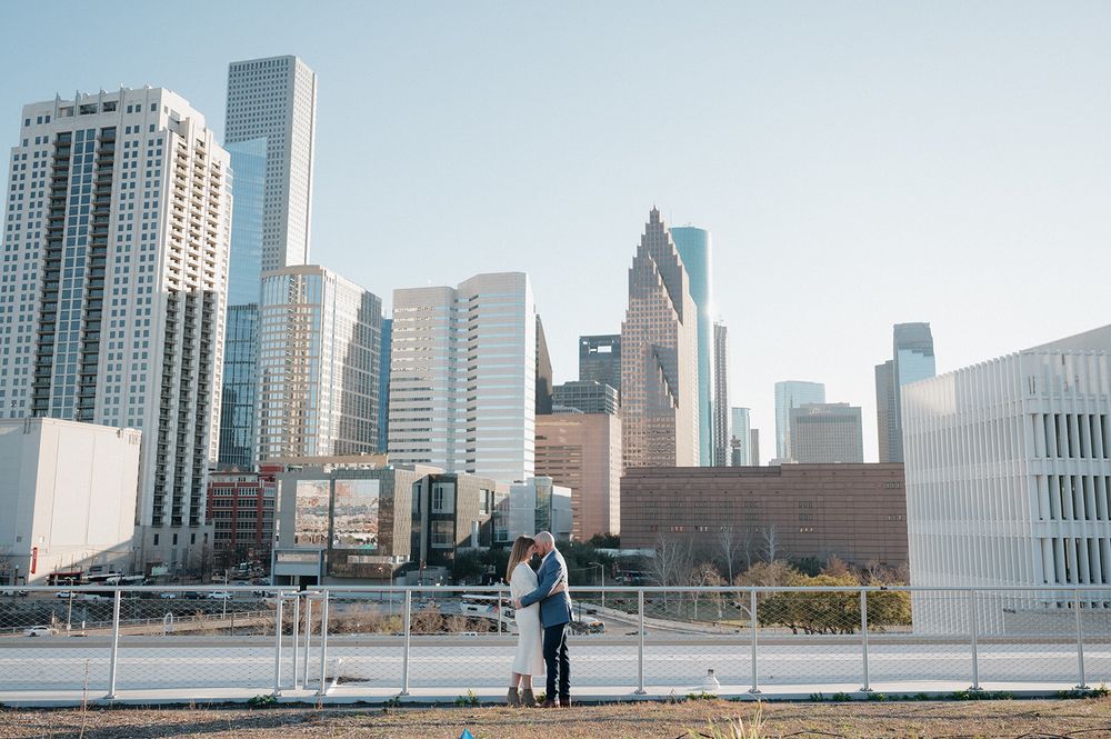 A couple stands on a viewing platform overlooking the downtown Houston skyline with tall modern skyscrapers in winter.