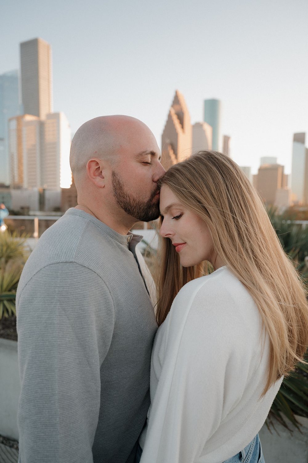 A couple shares an intimate moment against the backdrop of a city skyline at sunset.