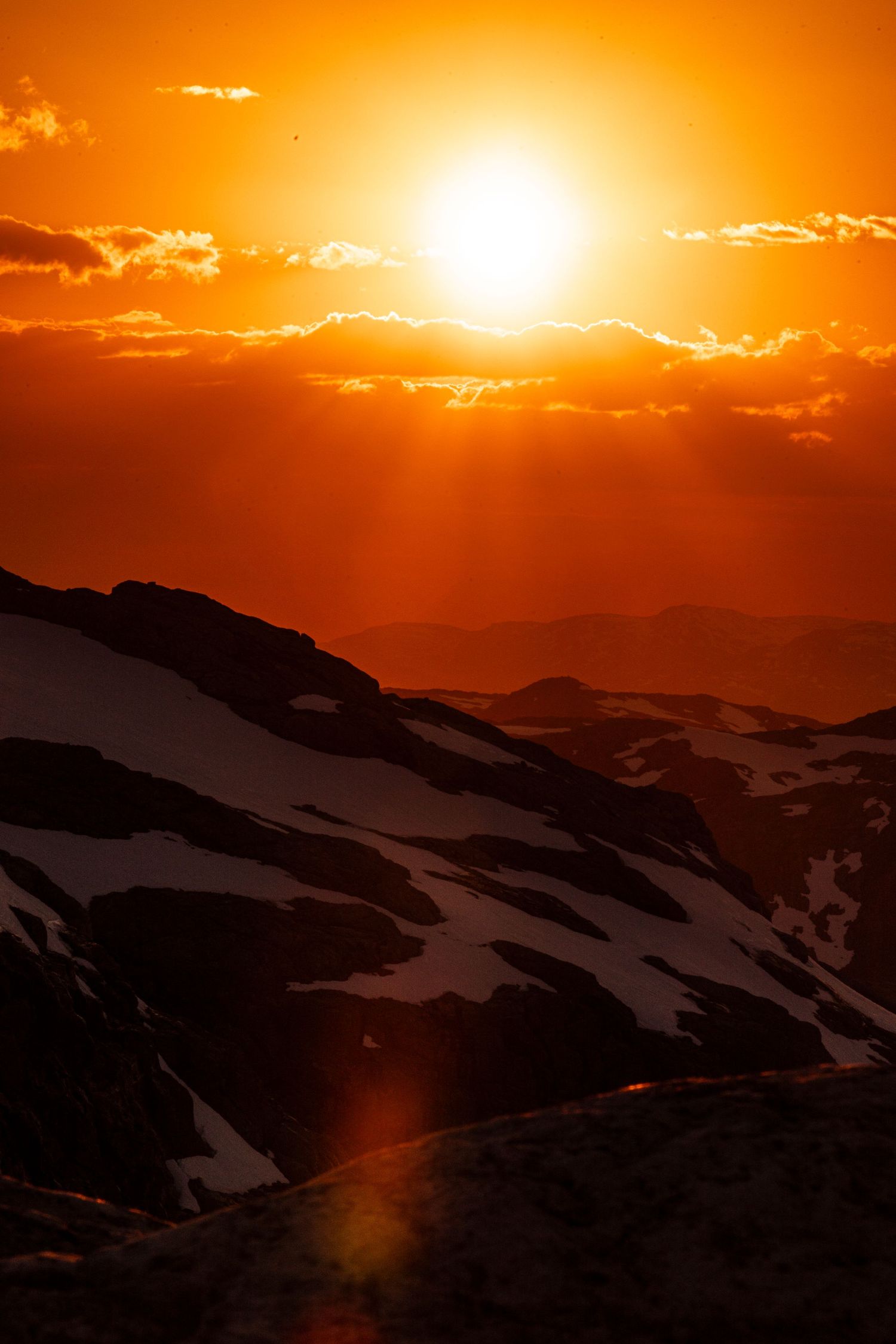 A dramatic orange sunset illuminates snowy mountain peaks with glowing clouds and silhouetted ridges in the background.