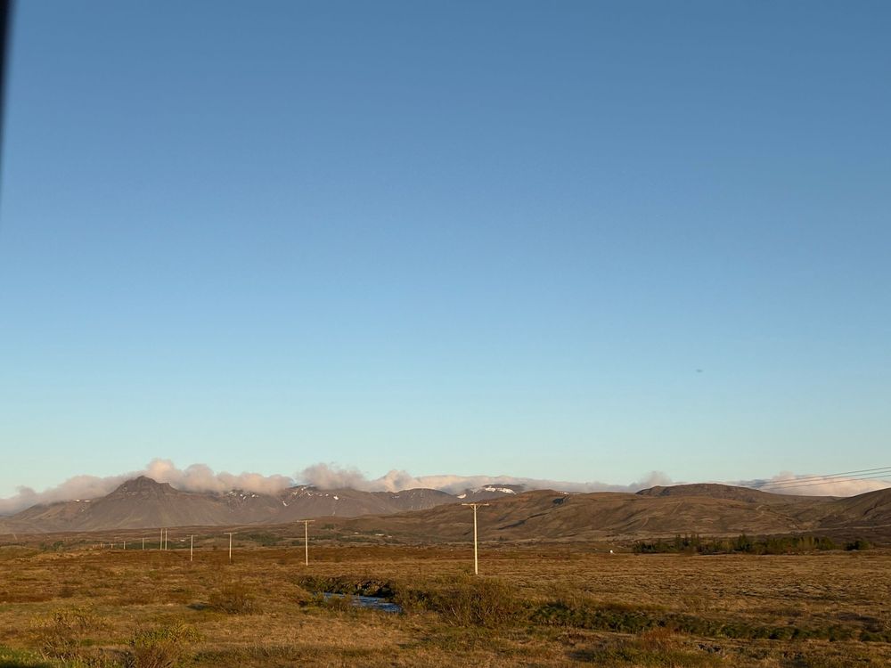 Power lines stretch across a rolling brown moorland landscape beneath distant mountains and blue sky.