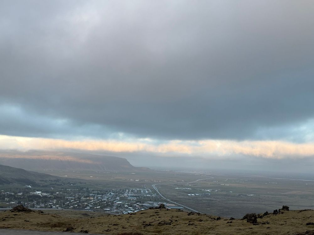 Dramatic cloudy skies over a valley town viewed from a mountainside during sunset.