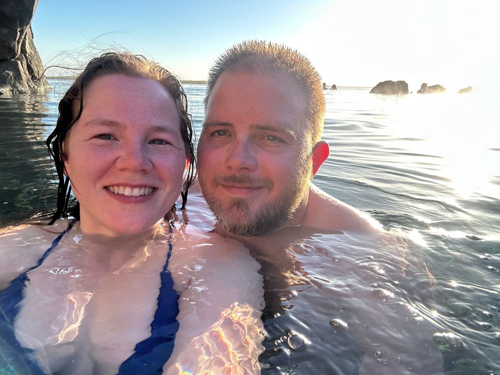 Two people smiling and enjoying a sunny day while swimming in calm waters together.
