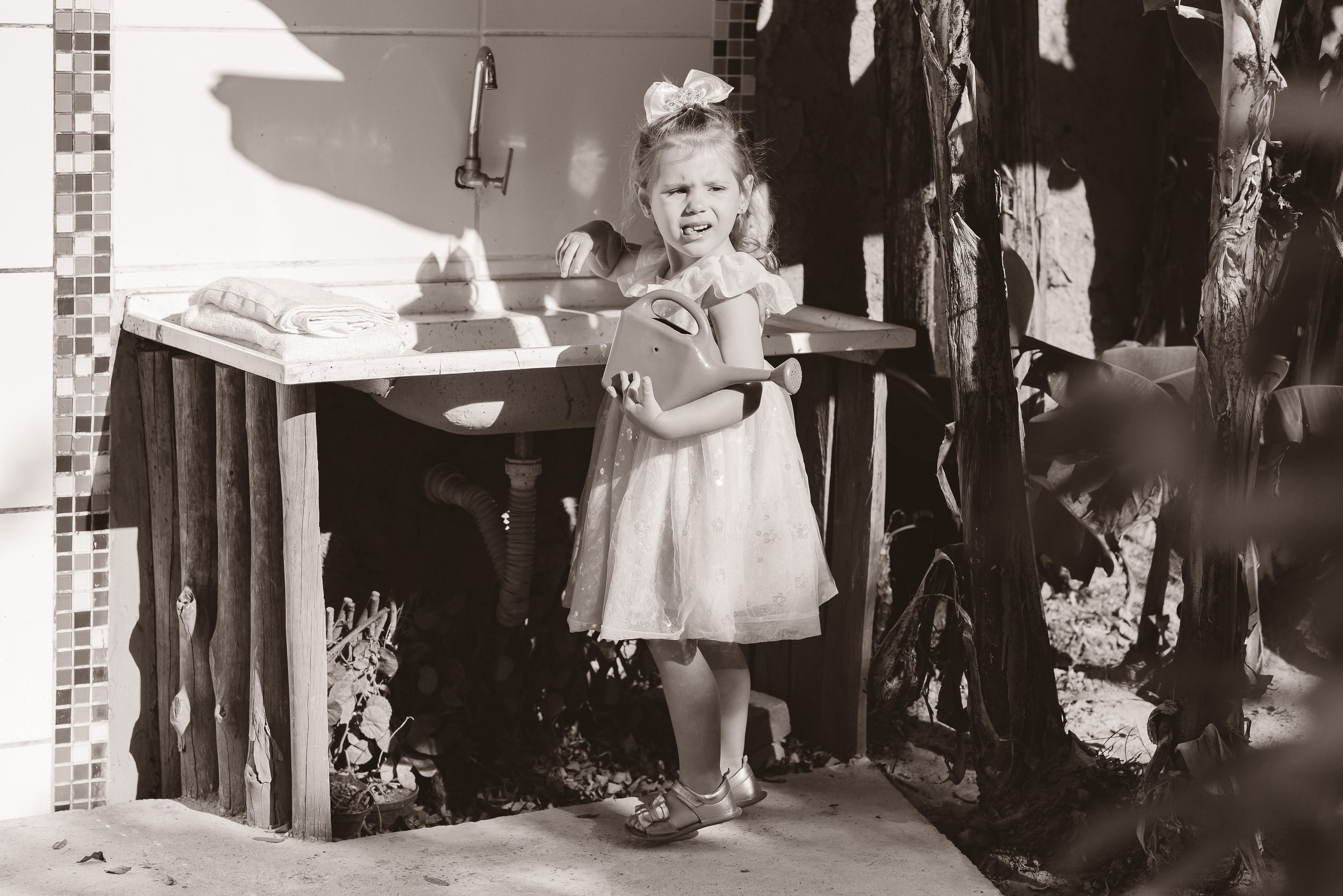 A vintage black and white photograph from the 1950s shows a small child in a white dress standing at a table outdoors.