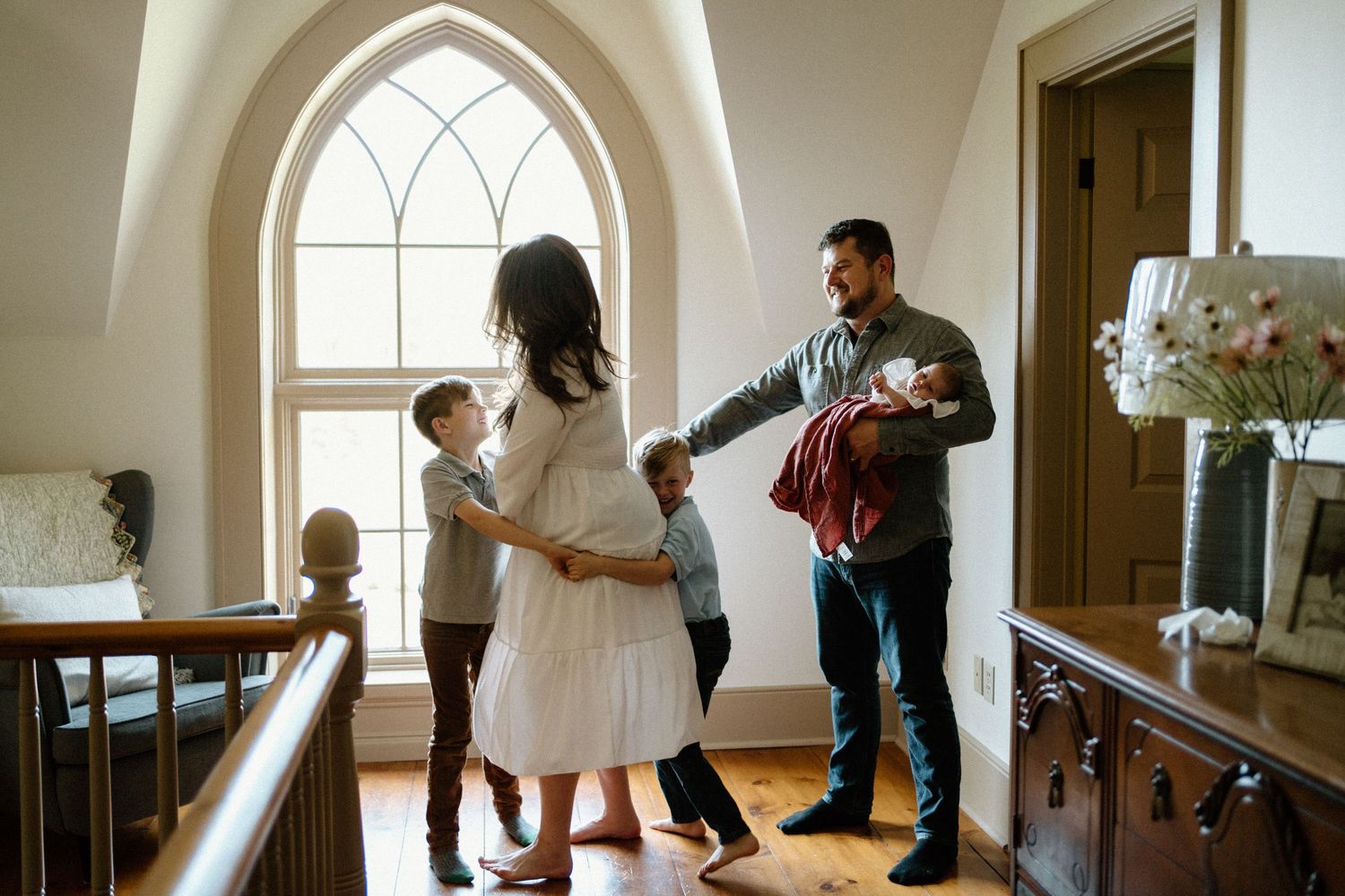 In a bright church room with an arched window, a family gathers together in an intimate moment near a floral arrangement.