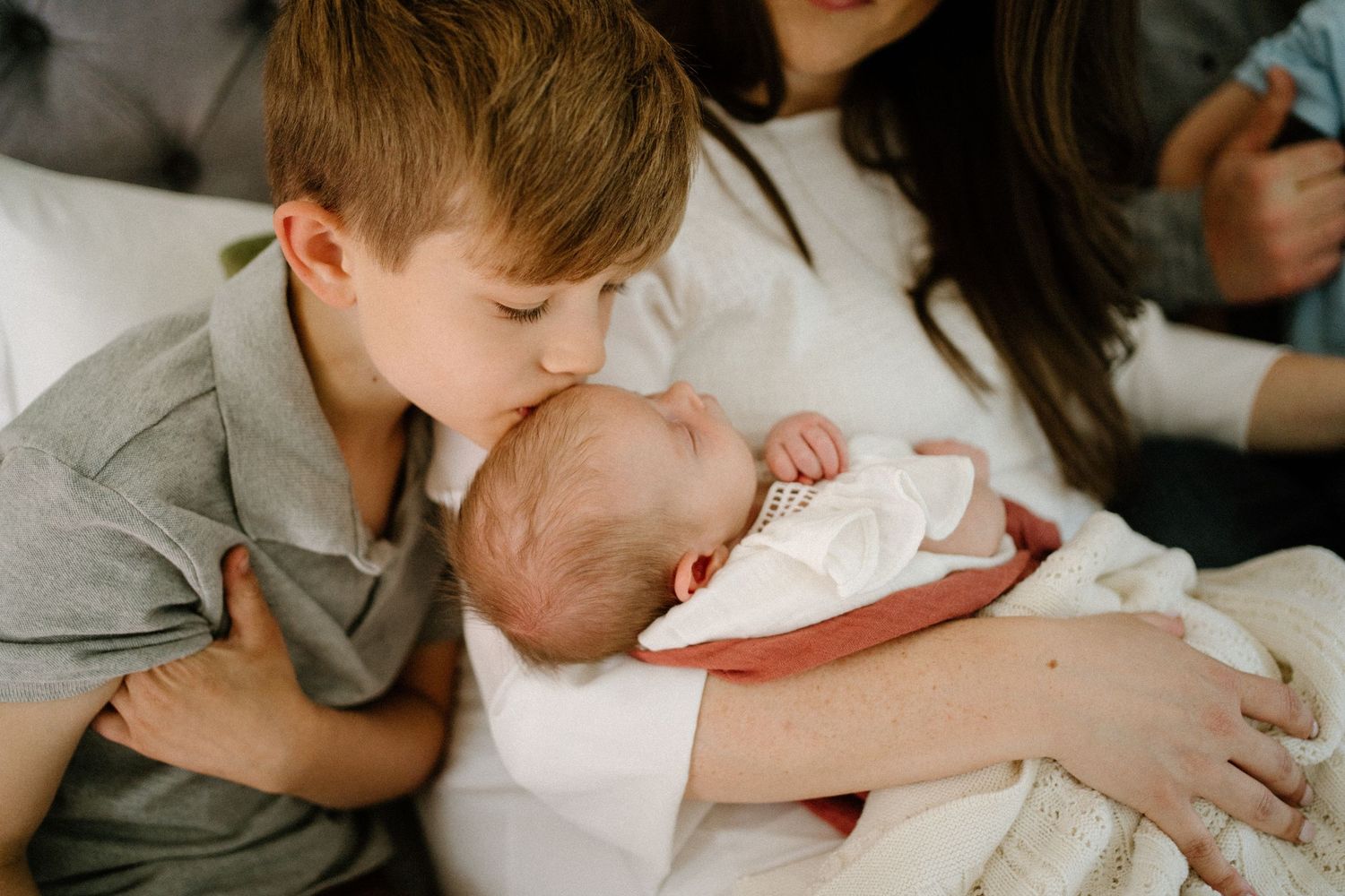 Young child giving a tender kiss to a sleeping baby wrapped in white swaddling.