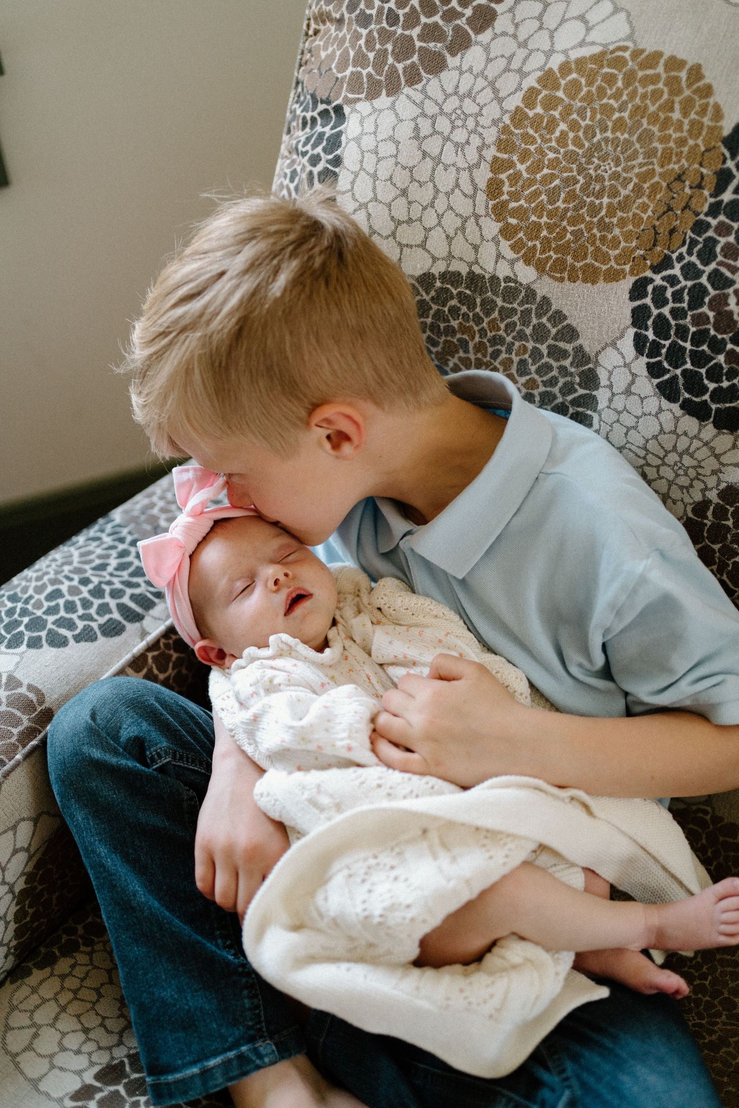 Sweet siblings share a tender moment on a patterned couch as older brother gives infant sister gentle affection.