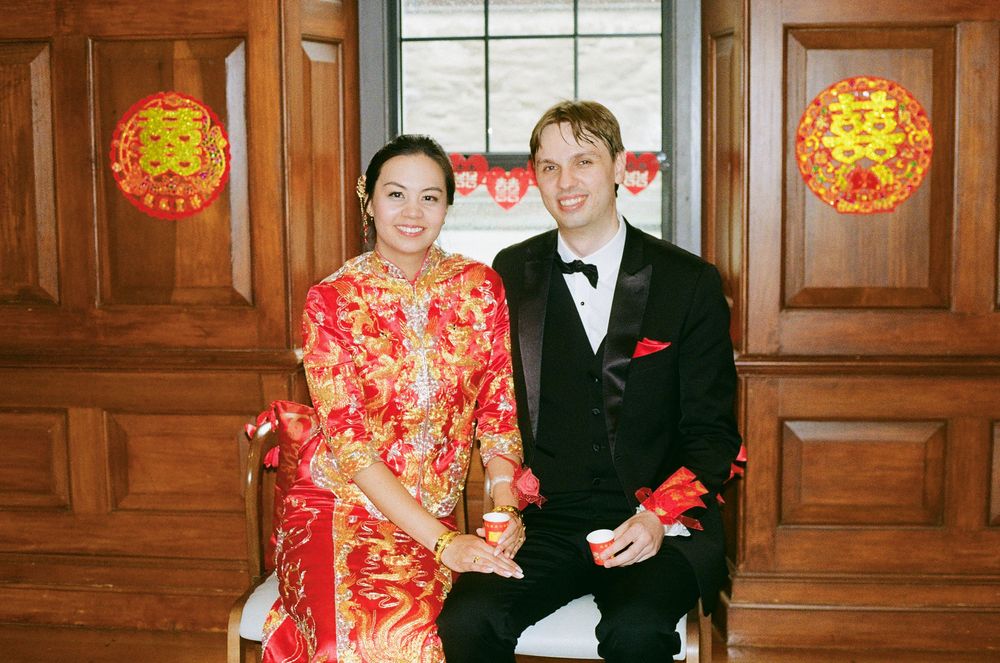 Newlyweds pose together against wooden paneling with red Chinese lanterns in the background.