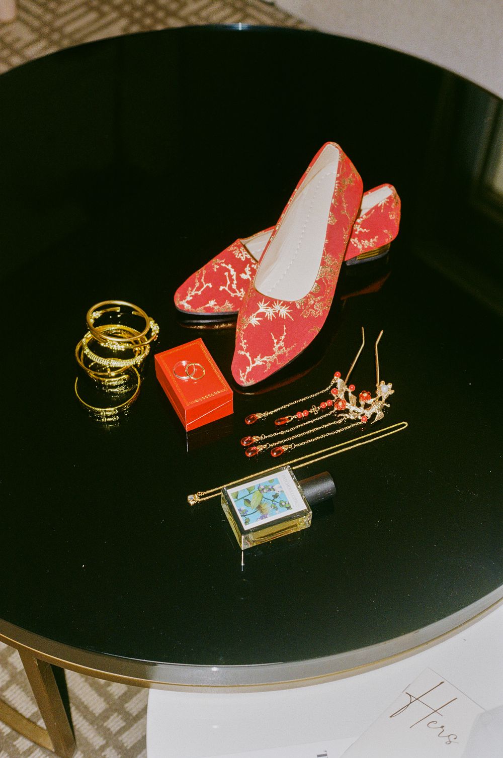Red bridal shoes and wedding accessories arranged on a black table.