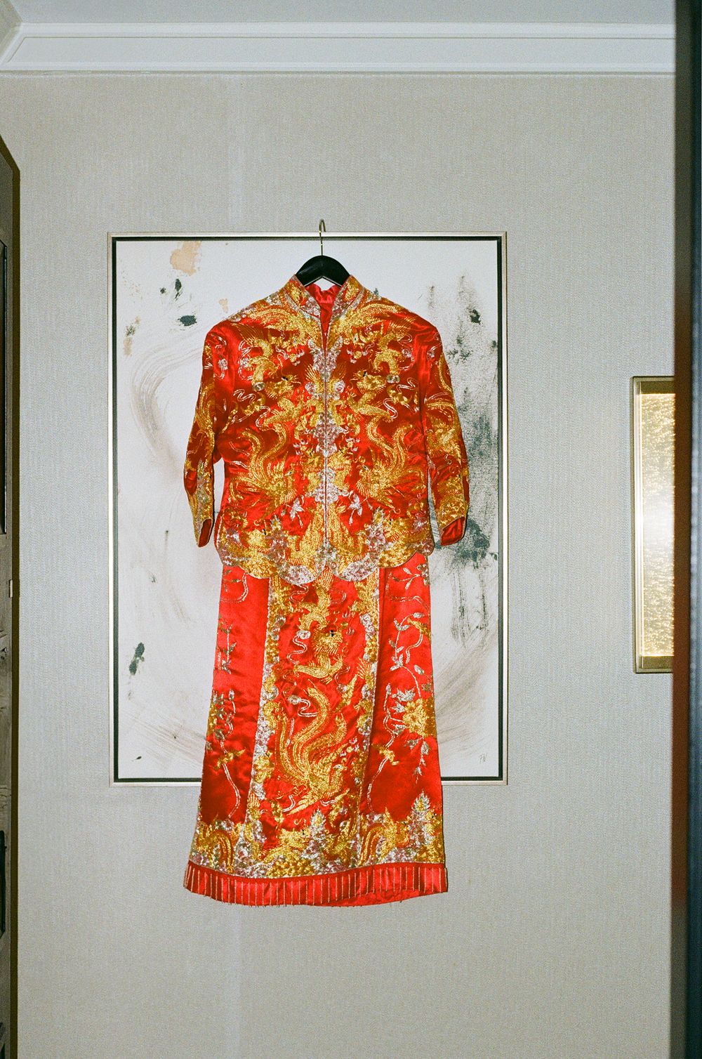 A traditional red Chinese wedding dress with gold embroidery displayed on a wall.