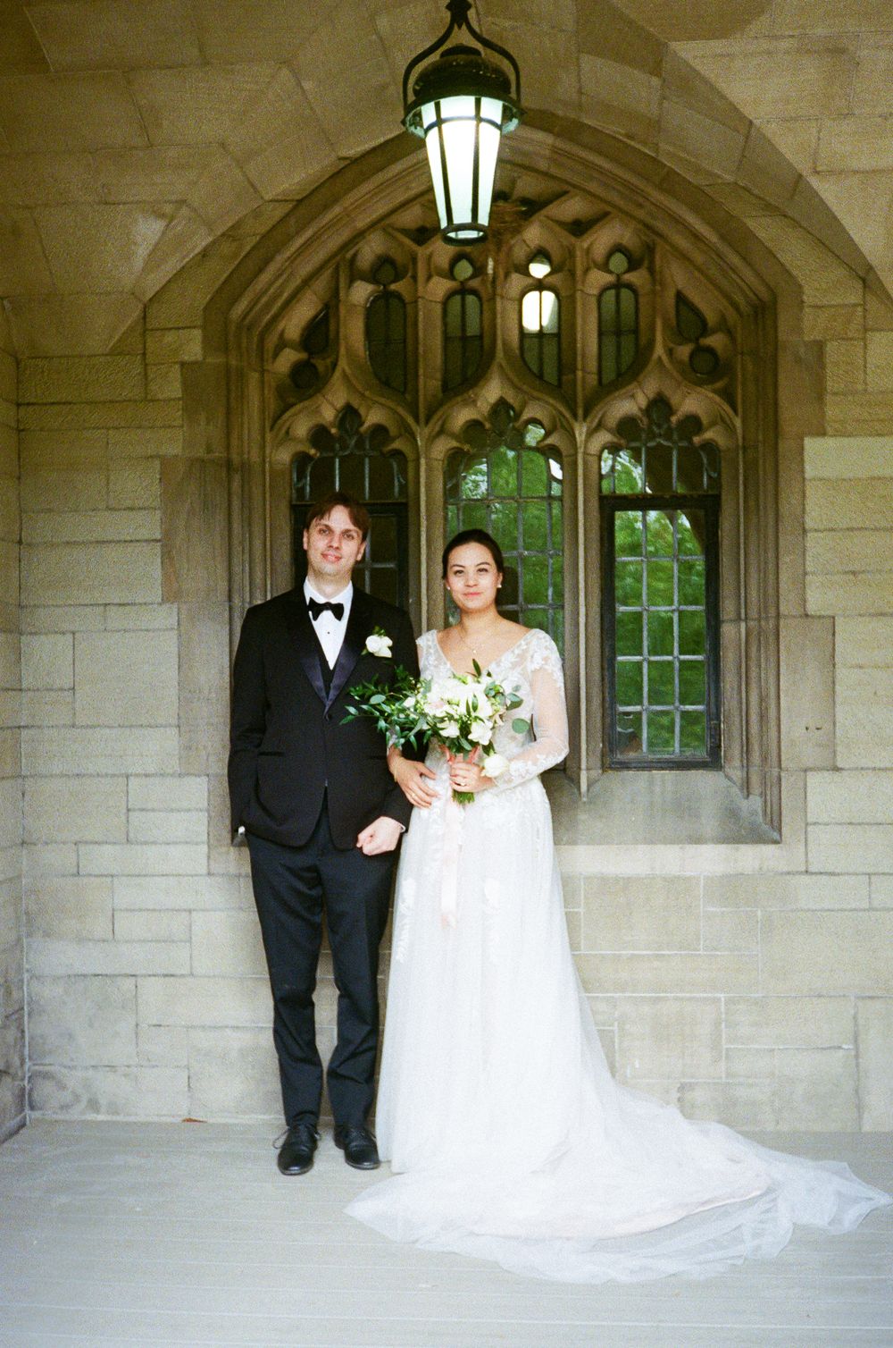 Gothic stone archway with ornate windows creates elegant backdrop for wedding portraits.