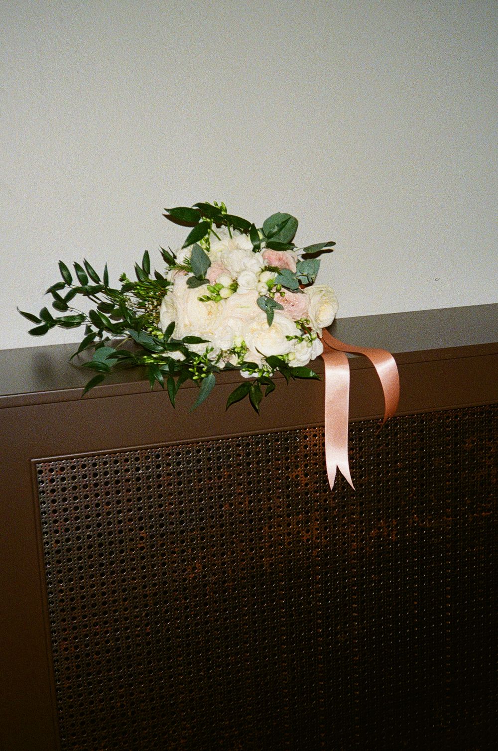 White floral arrangements with peach ribbons displayed on textured brown surface.