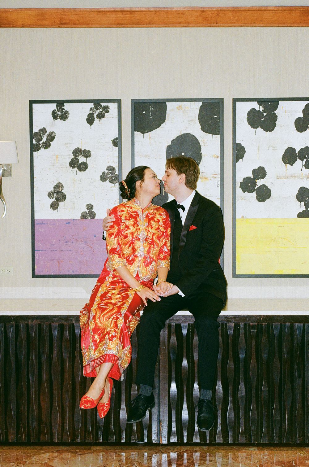 A couple in wedding attire sharing an intimate moment against a wall with artistic floral prints.