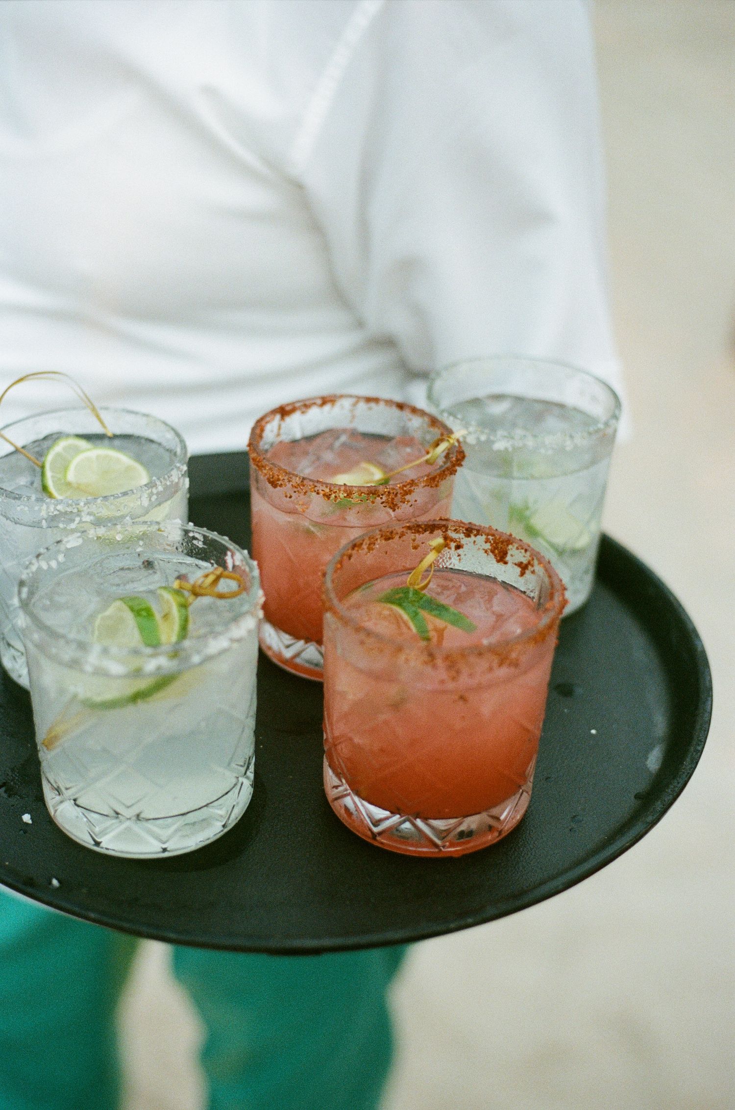 A serving tray with four cocktails garnished with lime and colorful rims.