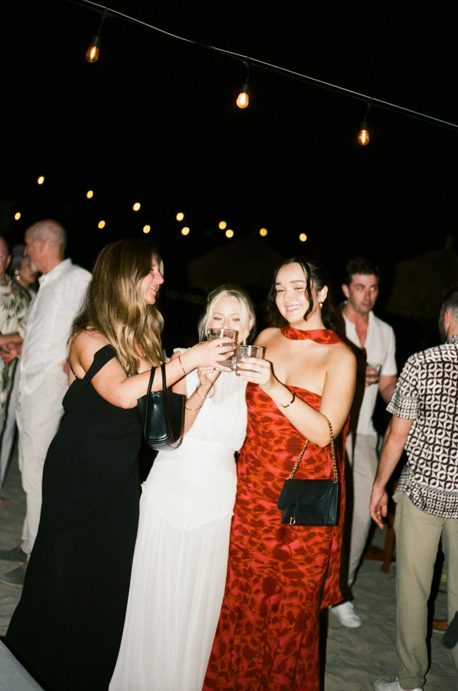 Party guests celebrating at a nighttime event under string lights on a beach.