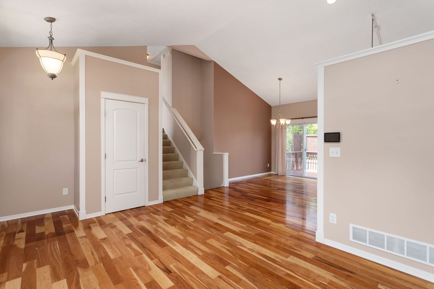 Modern open living space with hardwood floors, beige walls, and a staircase leading to the upper level.