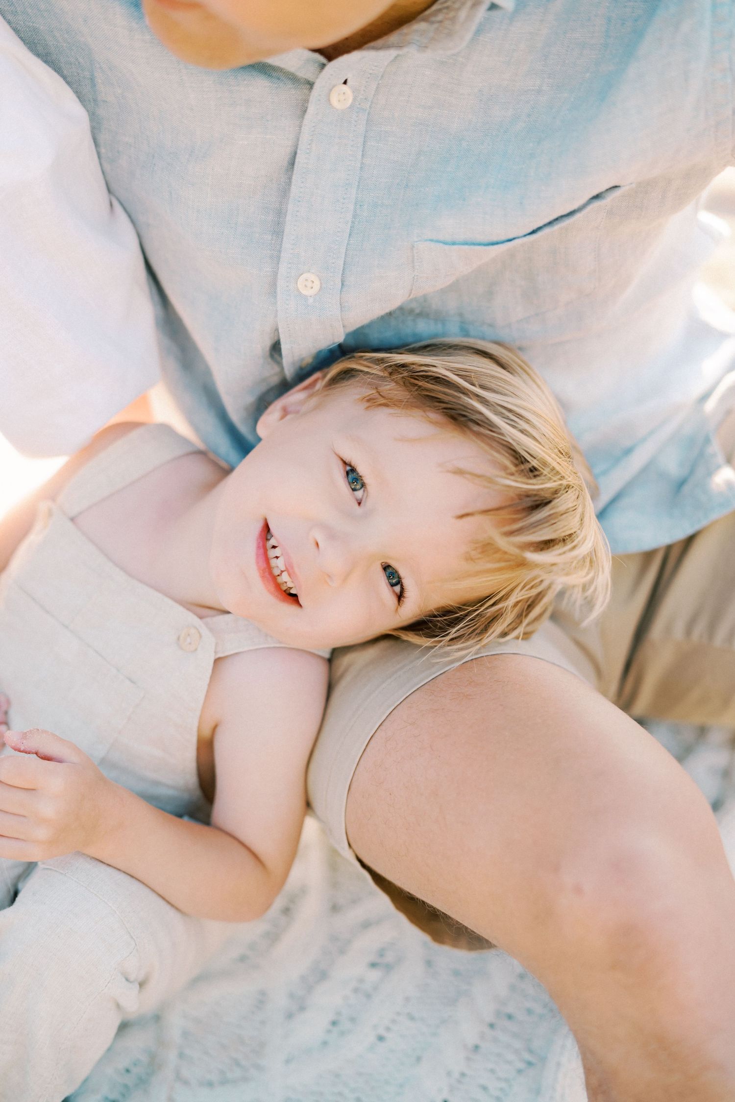 Close-up portrait of child laying back with bright smile against light blue background.