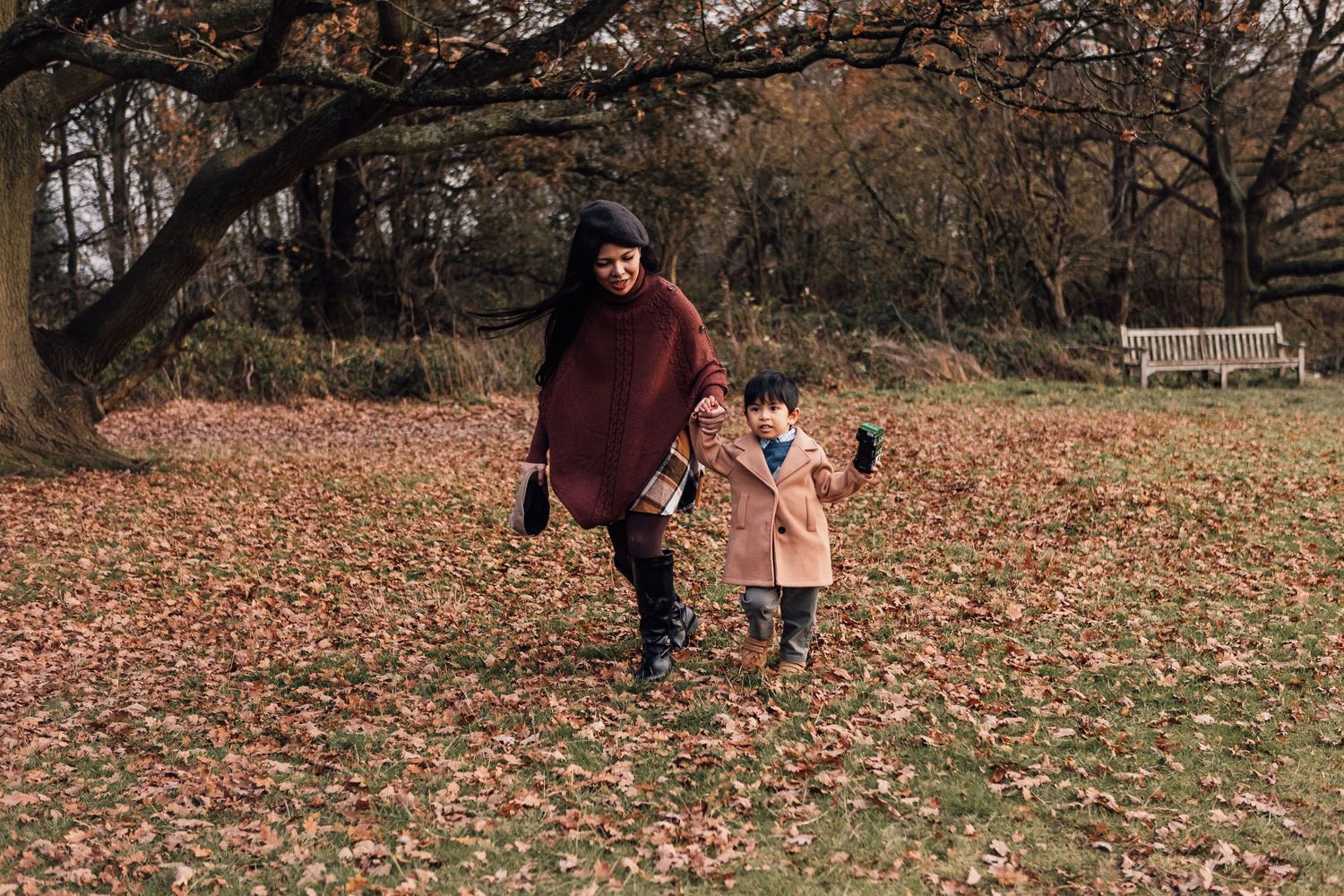 A parent and child walk together through fallen autumn leaves in a park on a crisp fall day.
