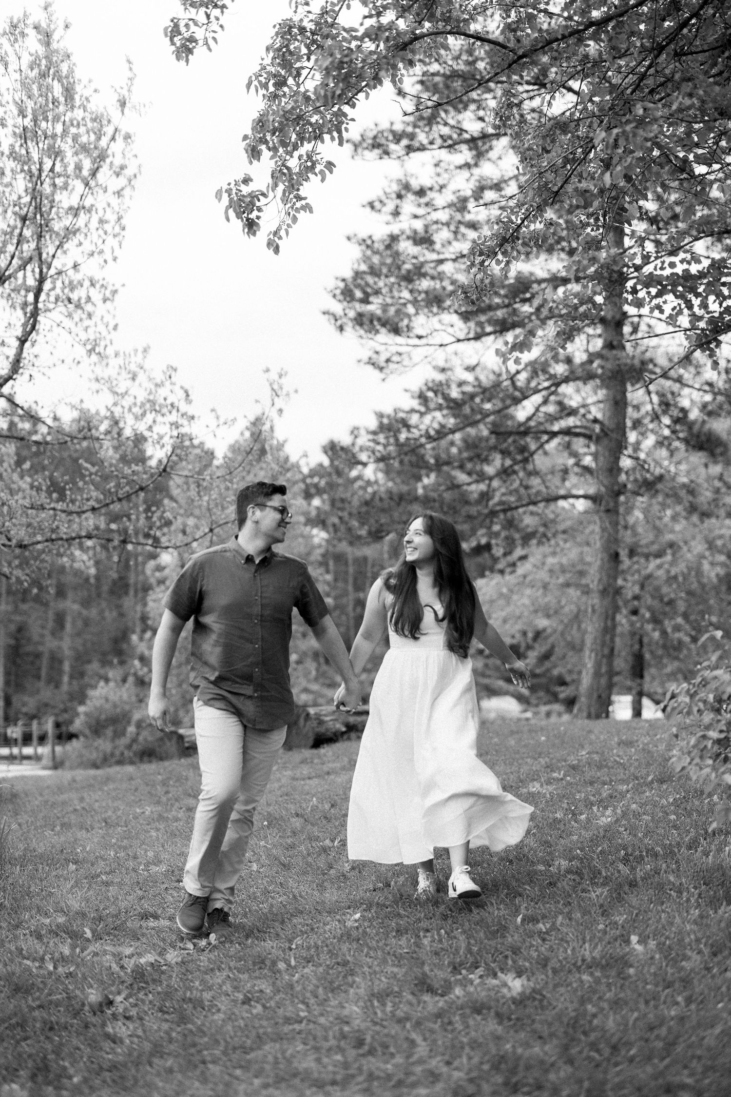 A couple walks together on grass while sharing a joyful moment in a black and white outdoor photo.