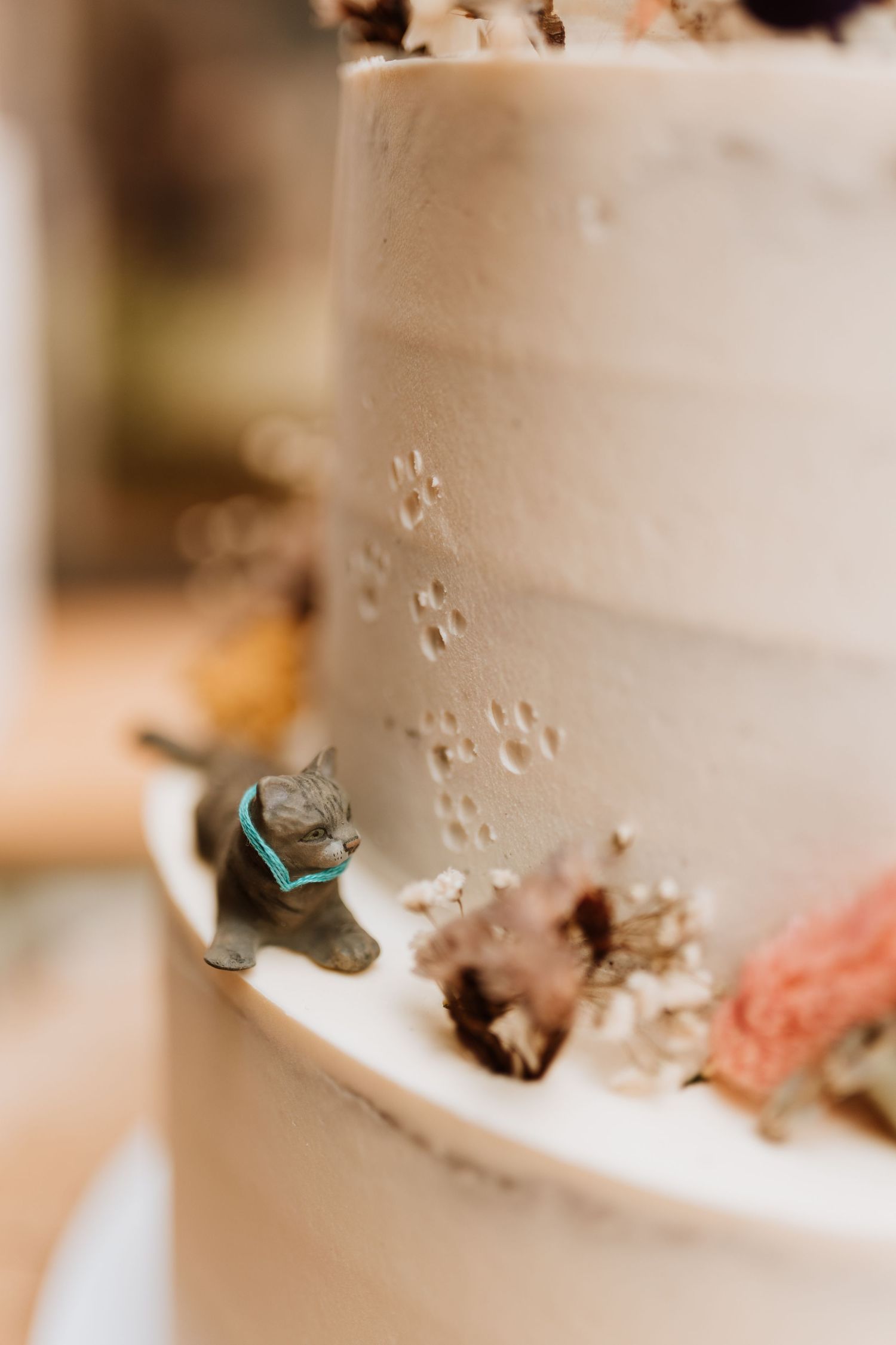 A small gray cat figurine adorns a white wedding cake decorated with delicate paw print patterns.
