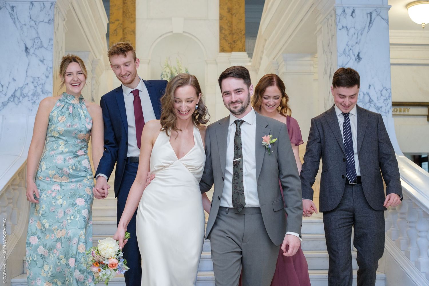 A wedding couple sits intimately together on ornate marble stairs with a white bouquet in a romantic moment.